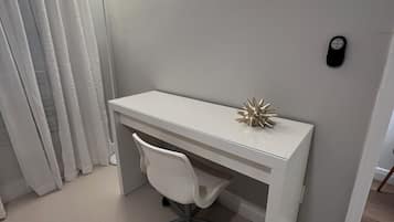 Een wit bureau met een stoel, een lamp en een decoratief object aan de muur.