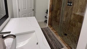 Un baño con un tocador blanco, cabina de ducha de vidrio y una puerta.