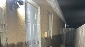 Un estrecho pasillo exterior con una puerta, un ventanal y una valla de madera.