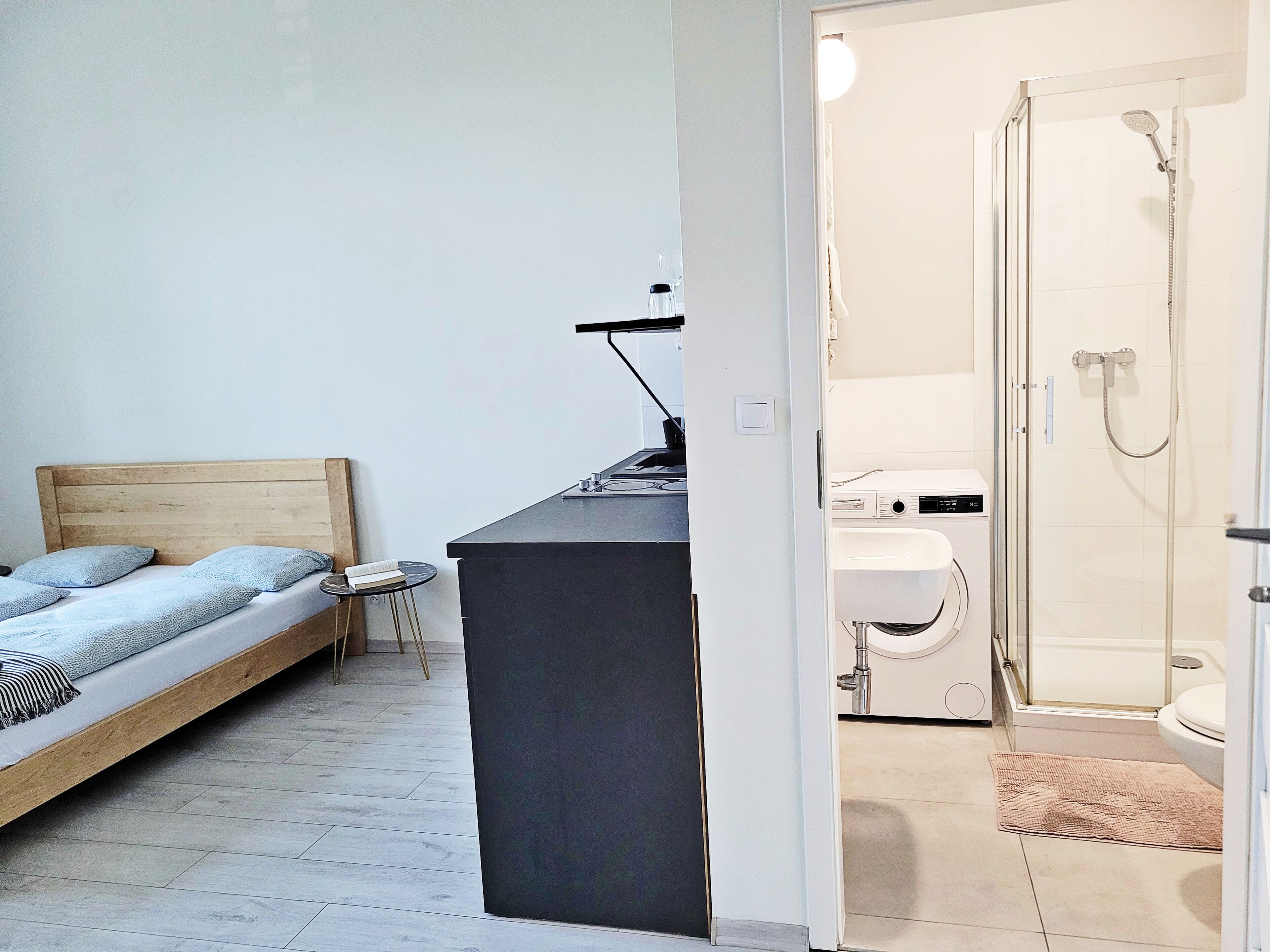A bedroom with a bed, a small table, and a kitchenette.