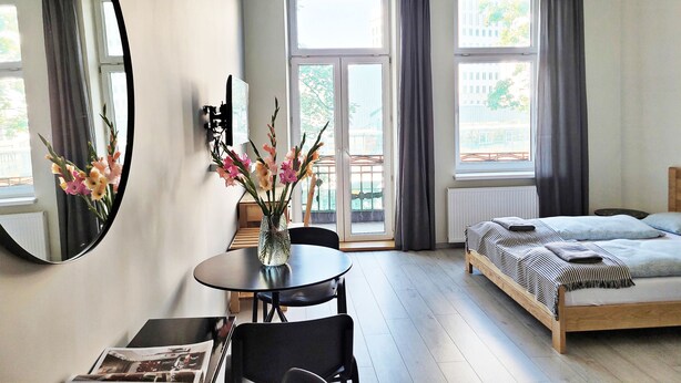 A modern bedroom with a bed, a round table with chairs, a large mirror, and a vase with flowers. - DReAM Main Station (Kraków)