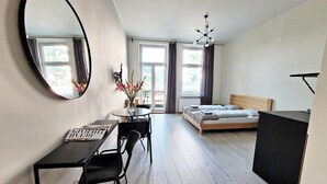 A modern bedroom with a wooden bed, a desk with a chair, a large mirror, and a vase with flowers. - DReAM Main Station (Kraków)