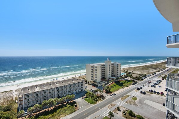 A coastal hotel with a view of the beach and ocean. It features multiple floors with balconies, a parking area, and a road leading to the beach. - Emerald Dolphin Unit 1520 (Pensacola Beach)