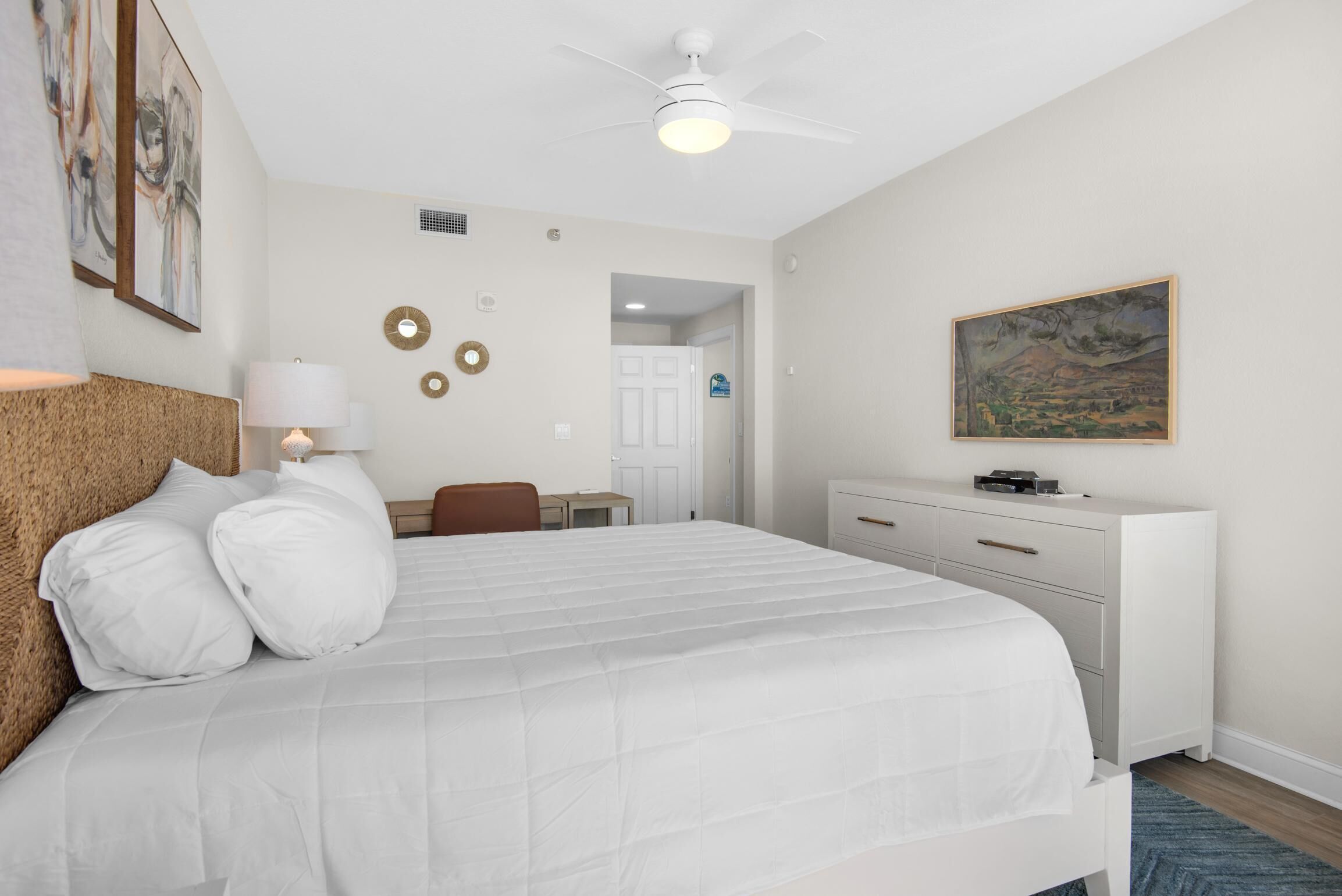 A bedroom with a bed, a desk, a chair, a dresser, and a ceiling fan.
