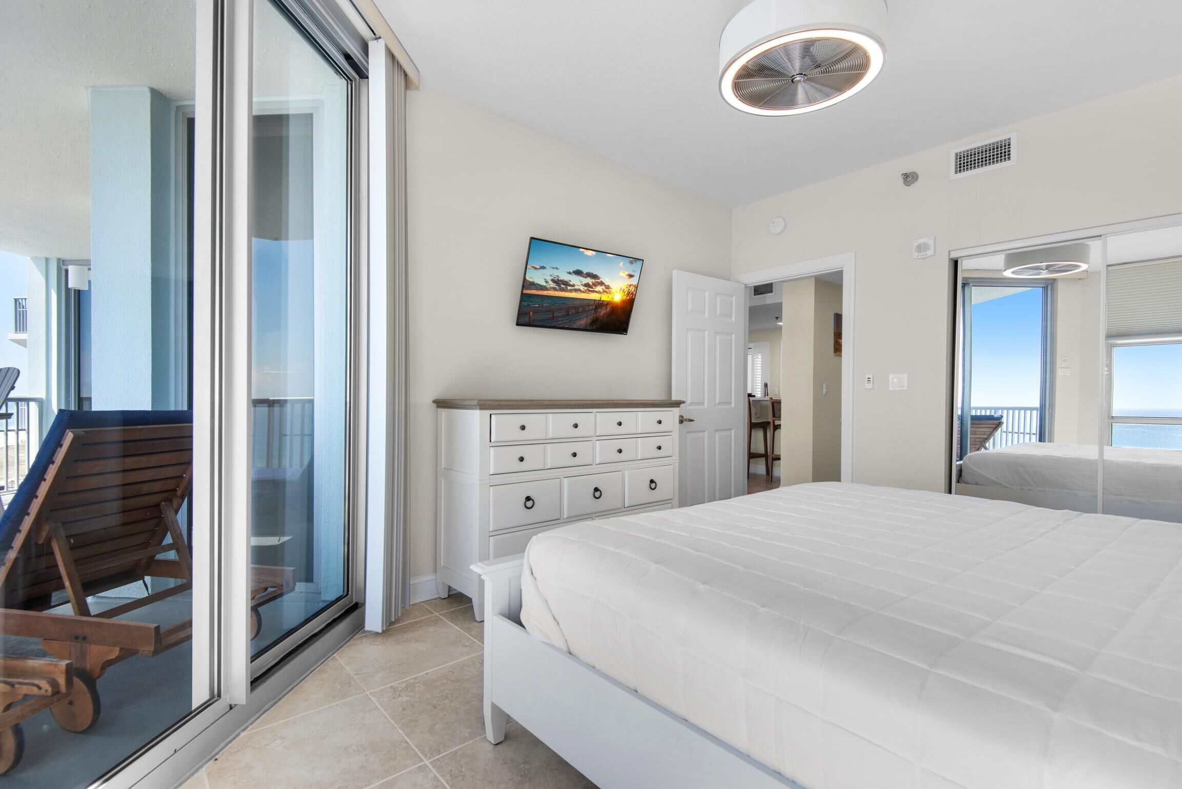 Een slaapkamer met een groot bed, een kaptafel, een stoel en een schuifpui naar een balkon.