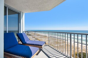 Ein Balkon mit zwei blauen Sitzgelegenheiten, der auf einen Strand hinausblickt.