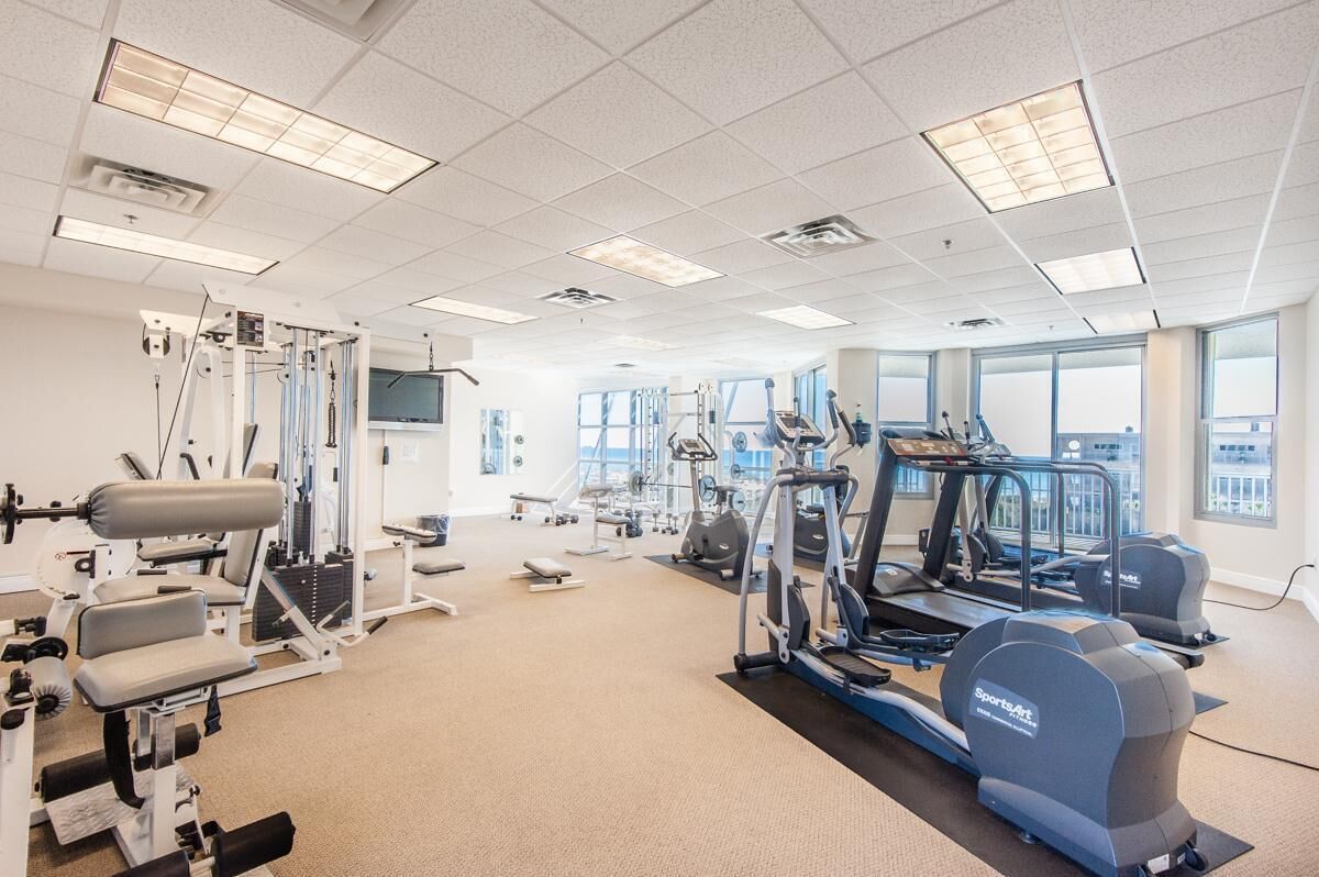 Une salle de sport équipée de machines de cardio, de matériel d’entraînement en force et dotée de grandes fenêtres.