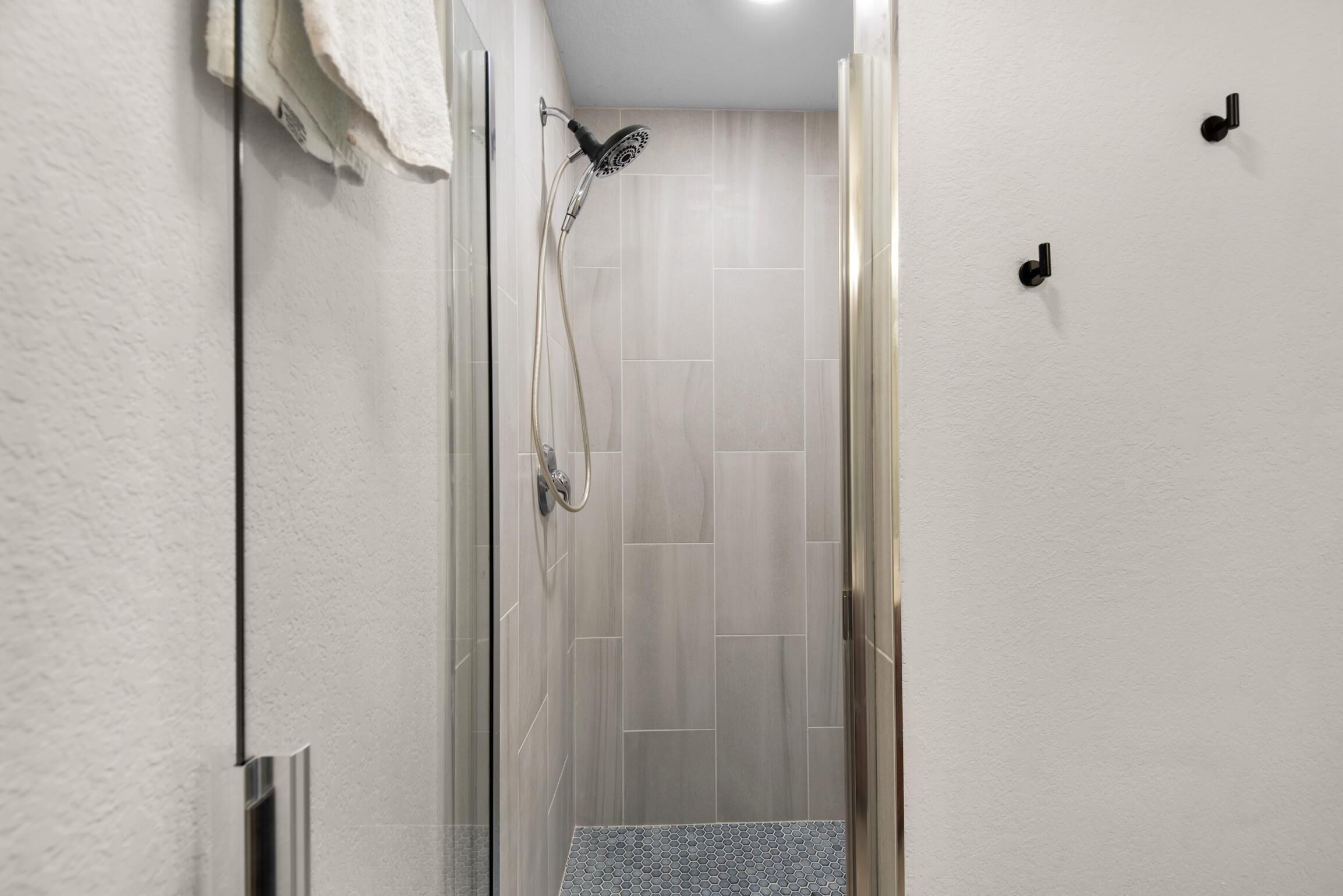 A modern shower area with a glass door, a handheld showerhead, and a tiled floor.