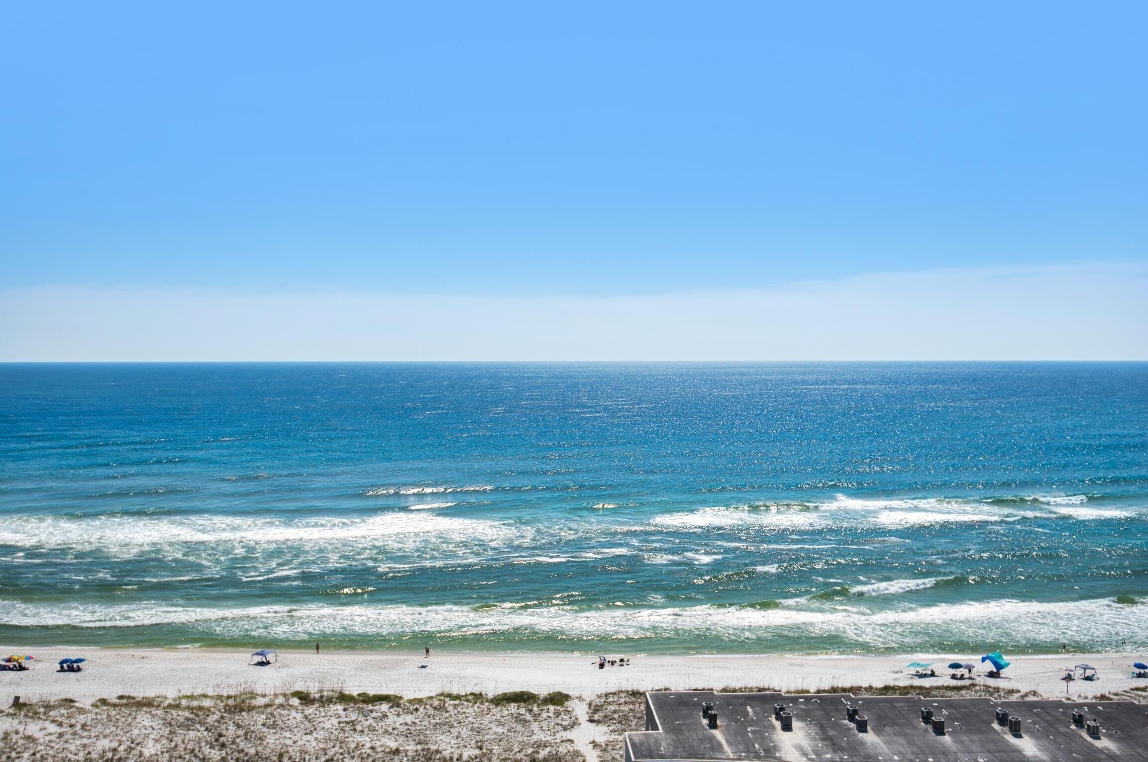 Une plage offrant une vue dégagée sur l’océan, une rive sablonneuse et un espace de stationnement où sont garés plusieurs véhicules.