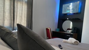 Hotelkamer met een bed, een afstandsbediening, een opgerolde handdoek, een bureau met een spiegel en een televisie waarop een welkomstboodschap staat.