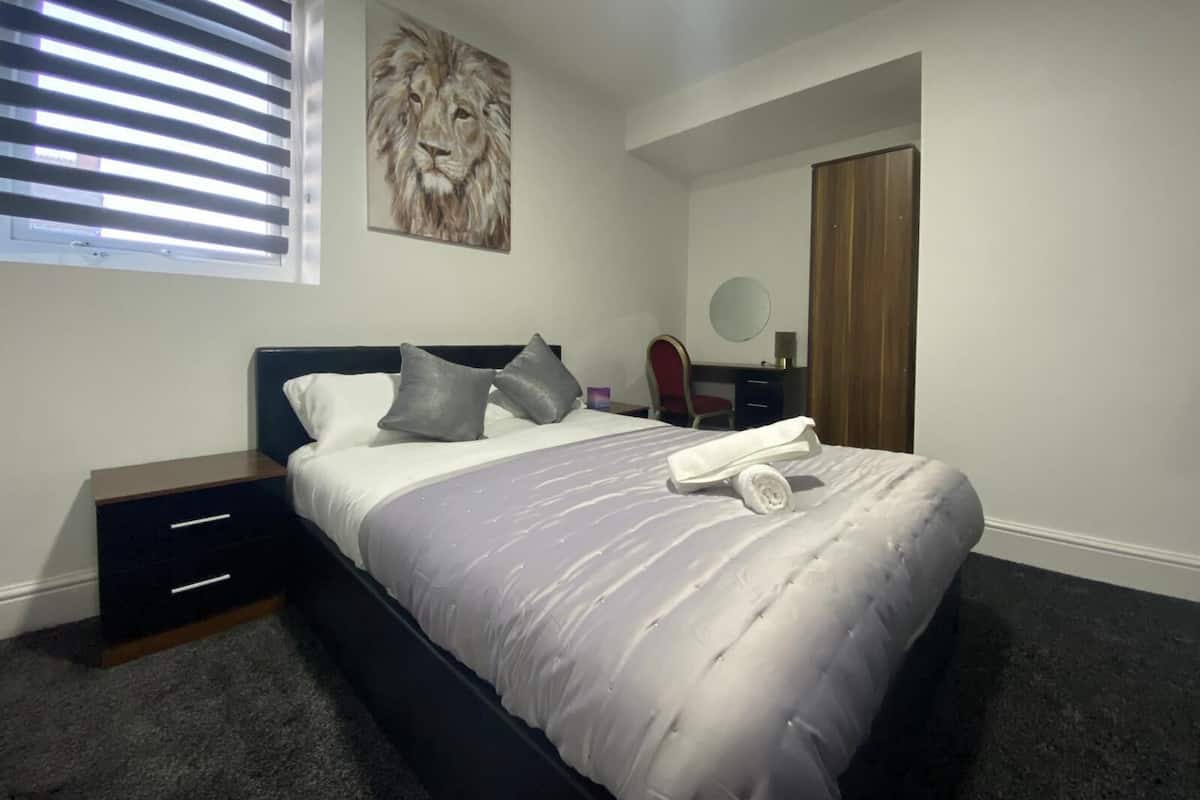 Une chambre à coucher comprenant un lit, une table de chevet, une commode, une fenêtre avec des stores, un tableau représentant un lion, un miroir et une porte.