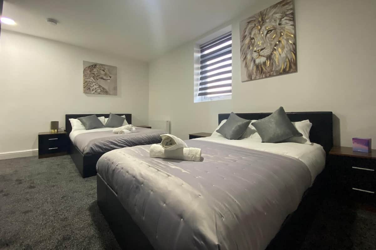 Une chambre double avec deux lits, une grande fenêtre avec stores et des œuvres d’art accrochées aux murs.