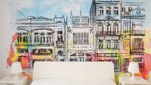 Ein Schlafzimmer mit einem großen Bett, zwei Nachttischen mit Lampen und einer farbenfrohen Stadtszenen-Mural an der Wand.