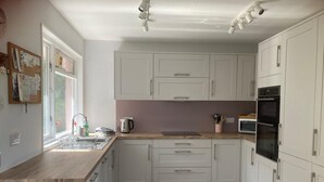 A kitchen with white cabinets, a wooden countertop, a sink, a kettle, and an oven.
