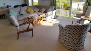 A living room with a sofa, two armchairs, a coffee table, and a view through large windows.