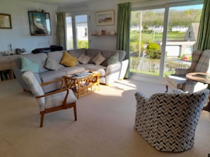 A living room with a sofa, two armchairs, a coffee table, and a view through large windows.