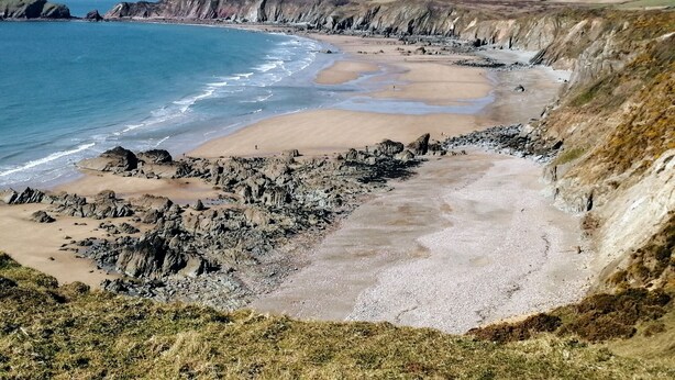 A coastal landscape with rocky cliffs, a sandy beach, and a clear blue sky.