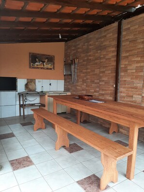 A kitchen with a wooden table, benches, a brick wall, and a tiled floor. - Pousada Recanto do Rosa (Imbituba)