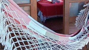 A hammock in a doorway leading to a room with a bed, a painting on the wall, and an air conditioning unit. - Pousada Recanto do Rosa (Imbituba)