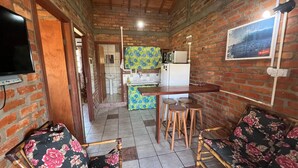A compact living space with a kitchen, dining area, and a TV mounted on the wall. - Pousada Recanto do Rosa (Imbituba)