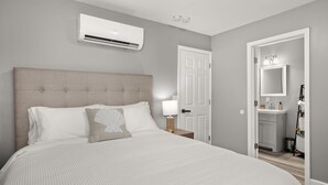 Une chambre à coucher avec un grand lit, un climatiseur, une lampe de chevet et une porte donnant sur une salle de bain.