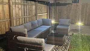 Une terrasse dotée de meubles en osier, d’un parasol et de guirlandes lumineuses.