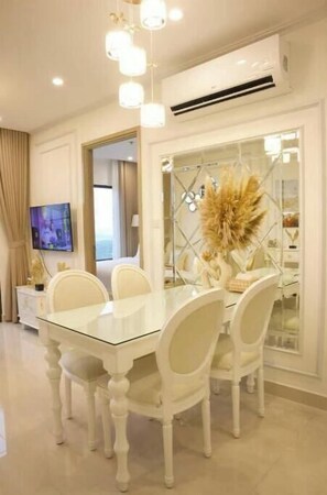 Enjoy meals at the glass-top dining table surrounded by six chairs, with a chandelier above and a large potted plant nearby.