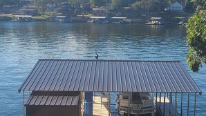 A dock with a covered seating area and a small building, overlooking a calm lake with houses in the background. - Lakeside home with Main Channel views (Sunrise Beach)