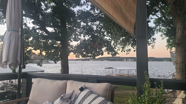 A covered outdoor seating area with a view of a body of water and distant buildings. - Lakeside home with Main Channel views (Sunrise Beach)