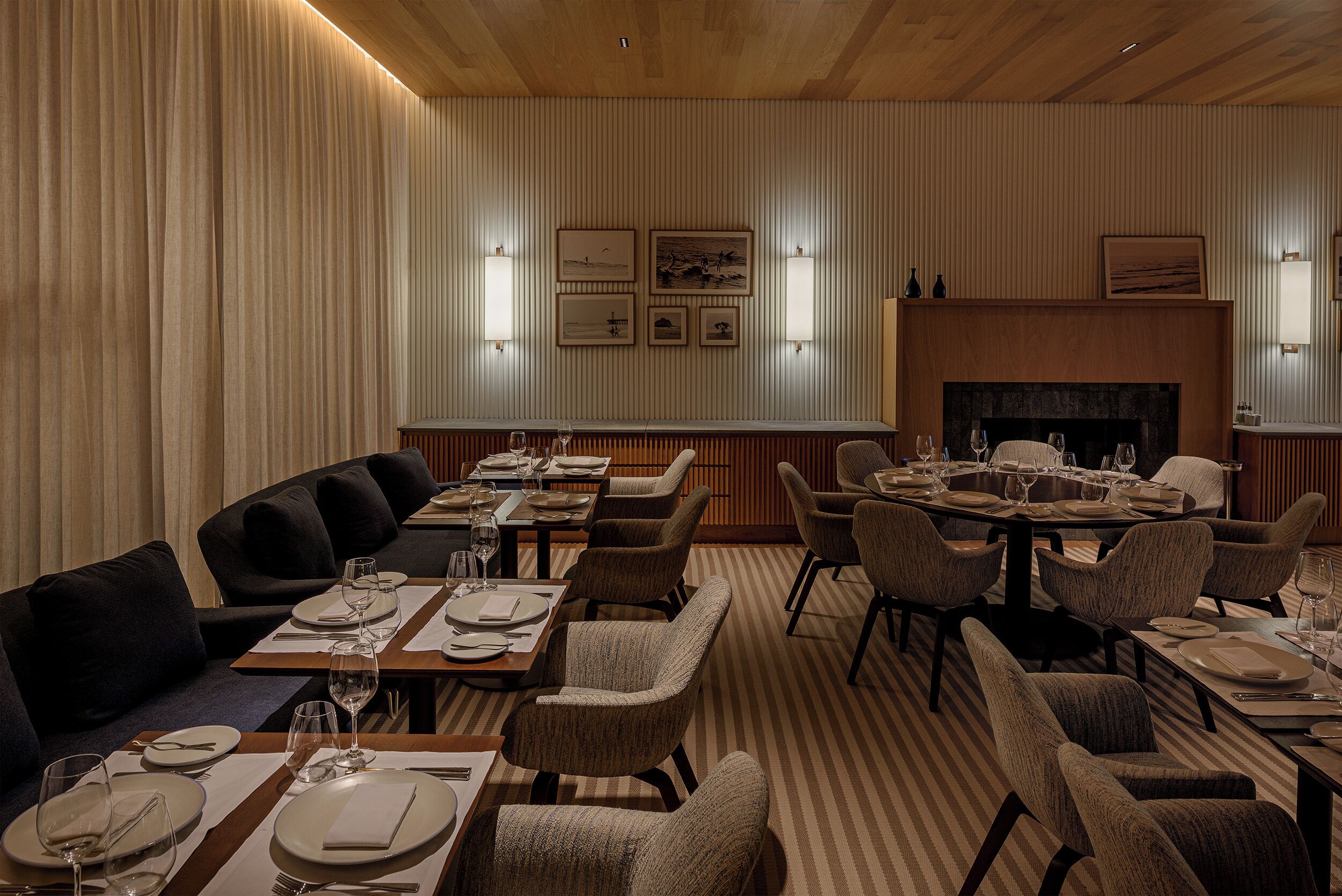 A dining area with tables set for four, cushioned seating, and a fireplace.