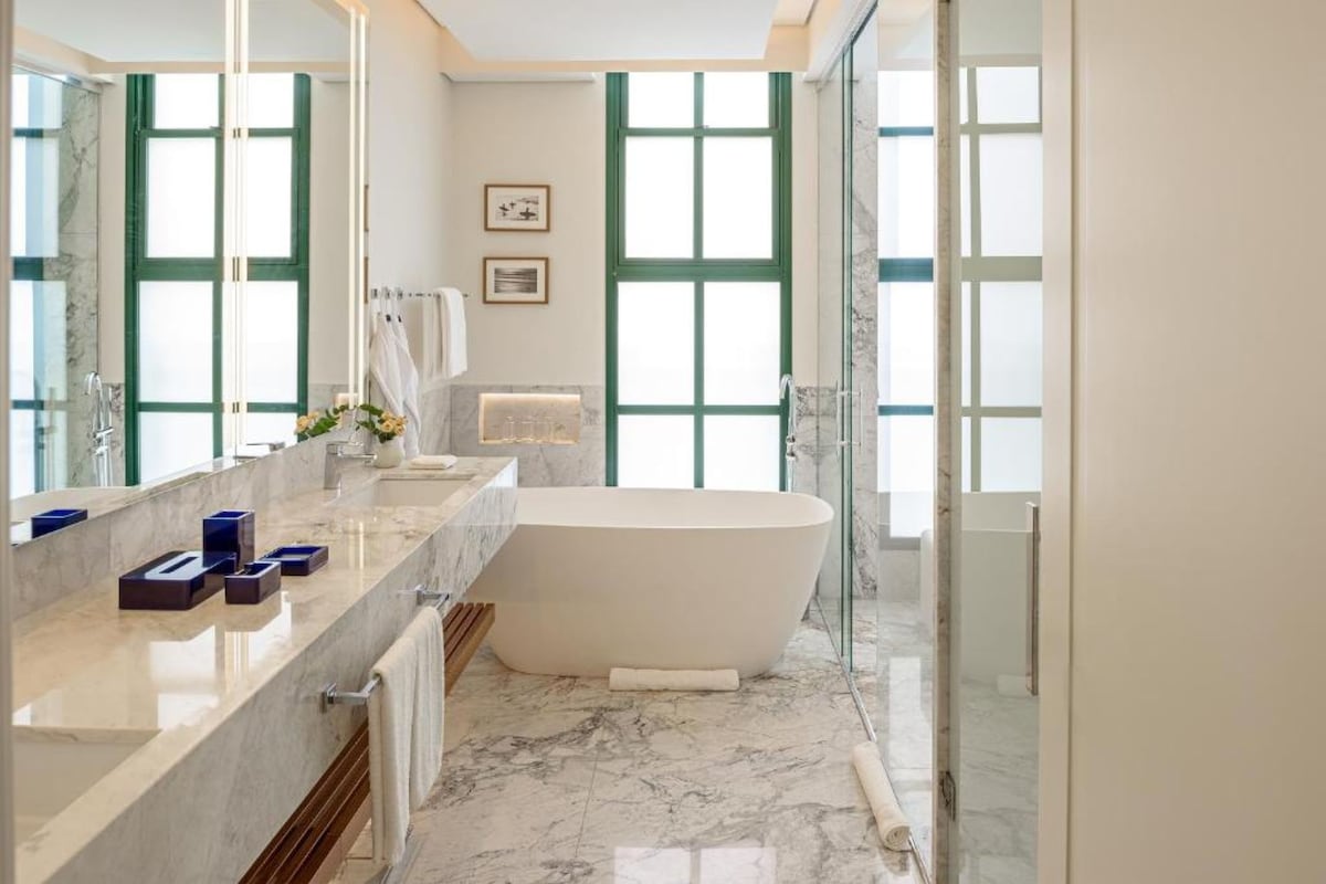 Un baño moderno con una bañera independiente, un espejo grande y suelo de mármol.