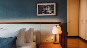 A hotel room with a bed, pillows, a bedside table with a lamp, a framed picture on the wall, and a wardrobe.