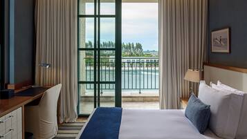 Habitación de hotel con cama, escritorio y silla, vista a un cuerpo de agua y edificios, y una ventana con cortinas.