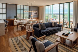 Quarto de hotel moderno com área de jantar, sofá e varanda com vista.