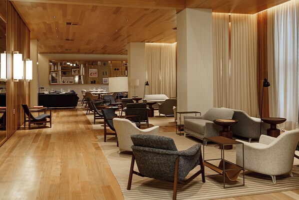 A spacious hotel lobby with wooden flooring, multiple seating areas, a reception desk, and a wall of framed pictures. - Boa Vista Surf Lodge (Porto Feliz)