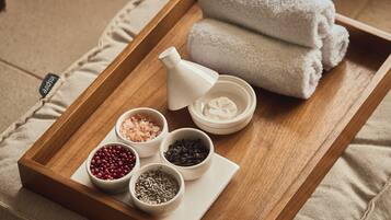 A wooden tray with bath salts, a bottle of oil, and rolled towels.