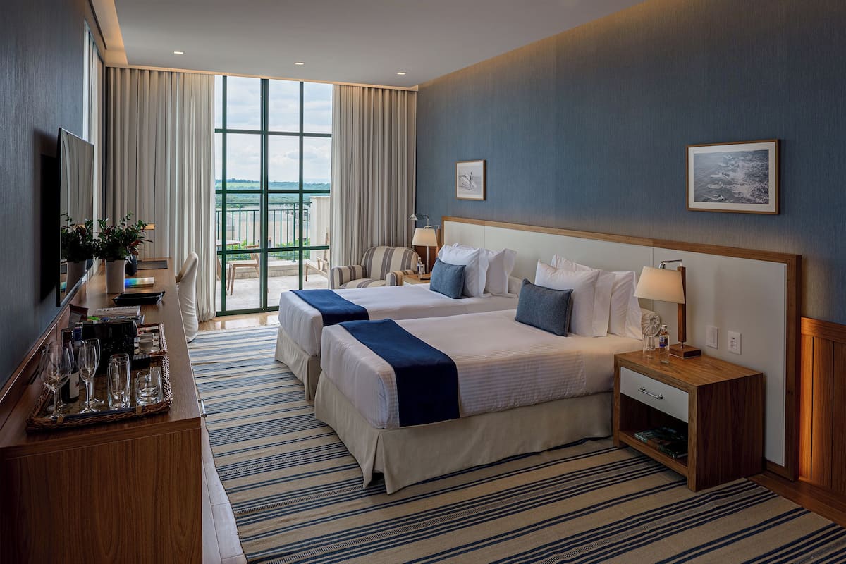 Een hotelkamer met twee bedden, een bureau met een computer, een televisie en een groot raam met uitzicht.