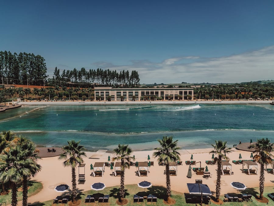 Un hotel frente a la playa con piscina, palmeras y vista al océano.