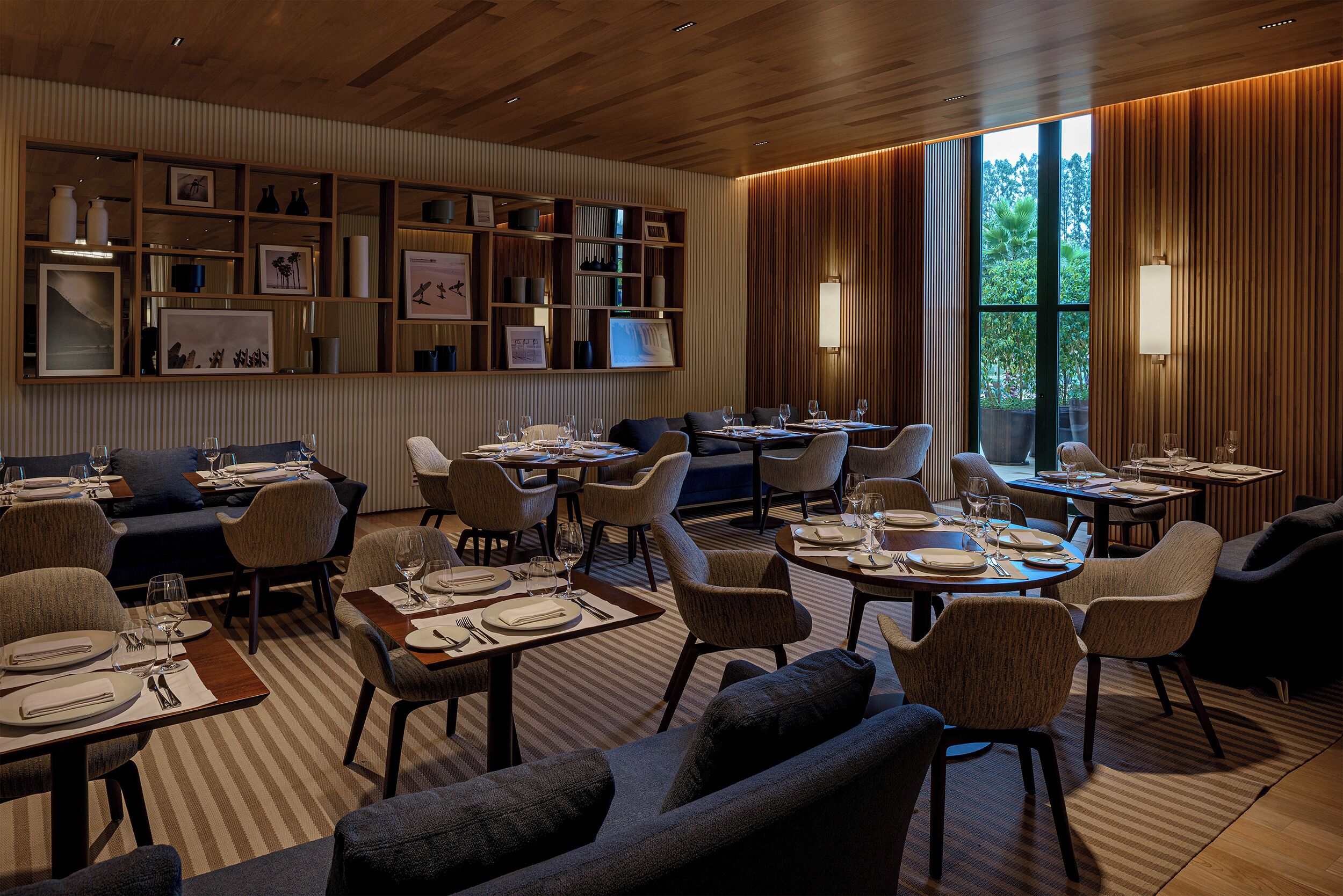 A modern dining area with multiple tables and chairs, a wooden ceiling, and a wall with framed pictures and decorative items.