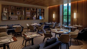 A modern dining area with multiple tables and chairs, a wooden ceiling, and a wall with framed pictures and decorative items.