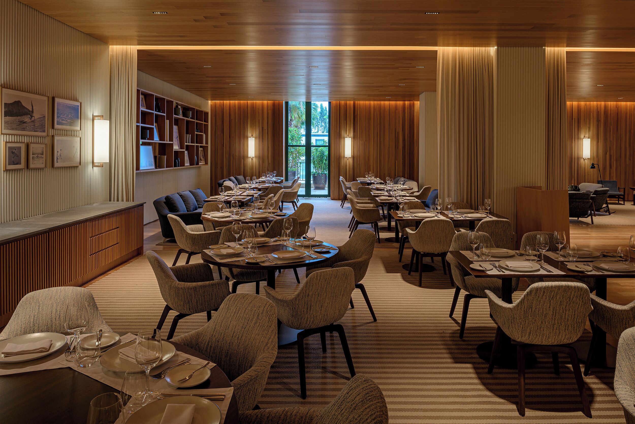 A spacious dining area with multiple tables and chairs, a long counter with a bar, and a view of greenery outside.
