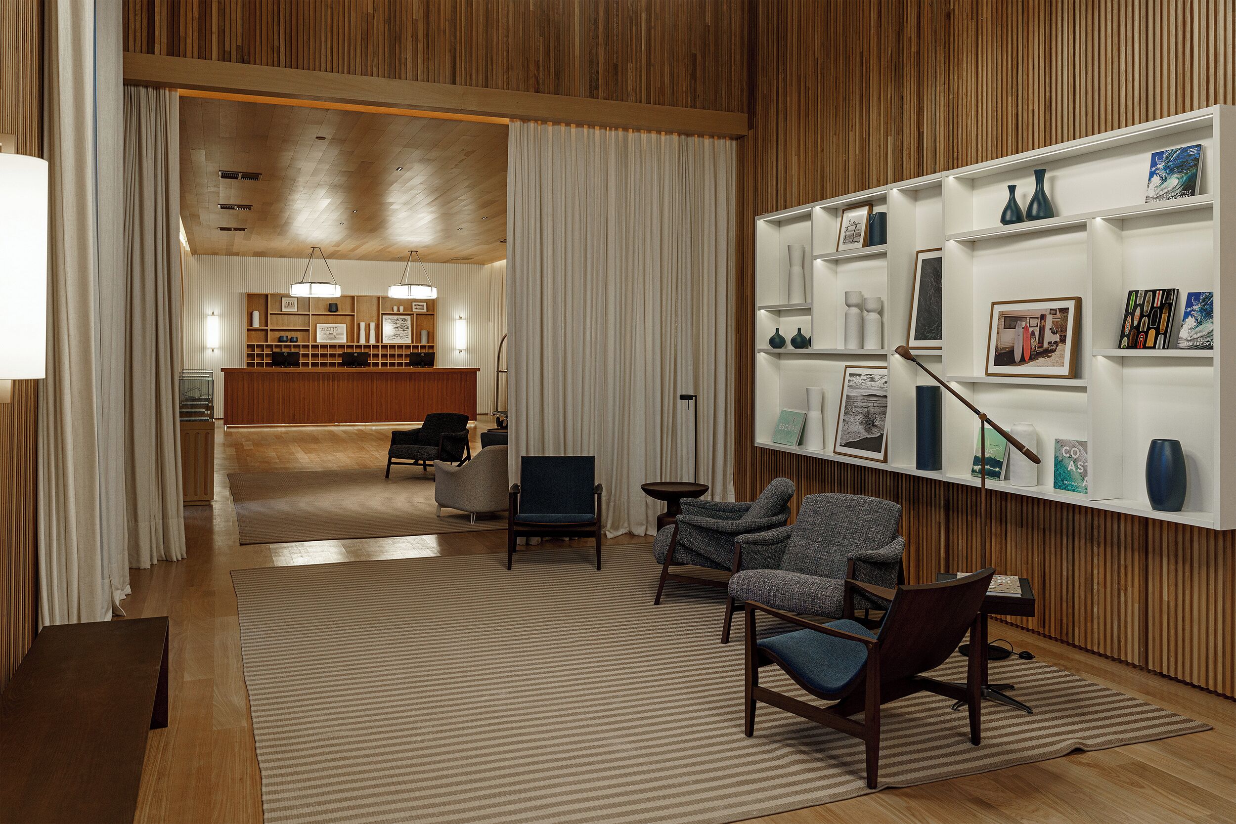 Un vestíbulo moderno con paneles de madera, mostrador de recepción, zona de estar con sillas y una pared con estanterías que exhiben diversos objetos.