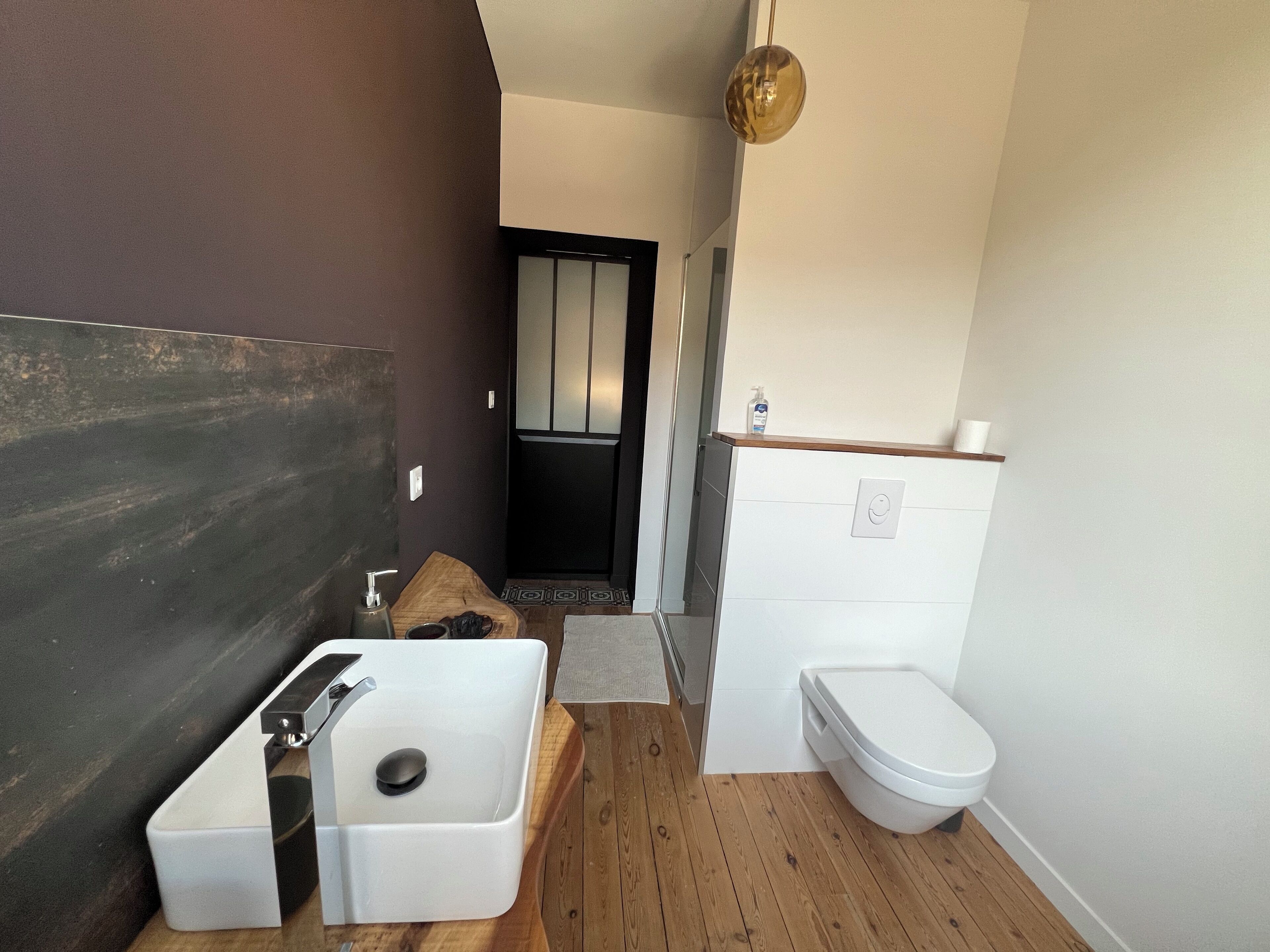 Un bagno compatto con lavandino bianco, mobile contenitore in legno, wc e un piccolo specchio.