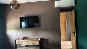 A room with a flat-screen TV mounted on the wall, a wooden cabinet below, and an air conditioning unit on the wall. - Aux Deux Tours (Leval)