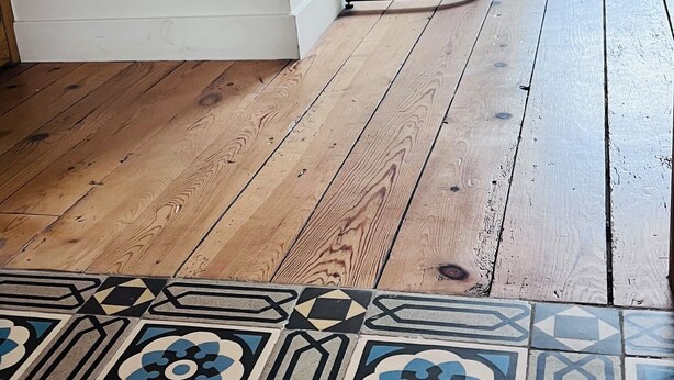 A room with a wooden floor, a patterned rug, and a black metal table against a white wall. - Aux Deux Tours (Leval)