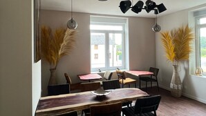 A dining area with a wooden table, chairs, and two large vases with pampas grass. There are pendant lights and a ceiling light fixture. - Aux Deux Tours (Leval)
