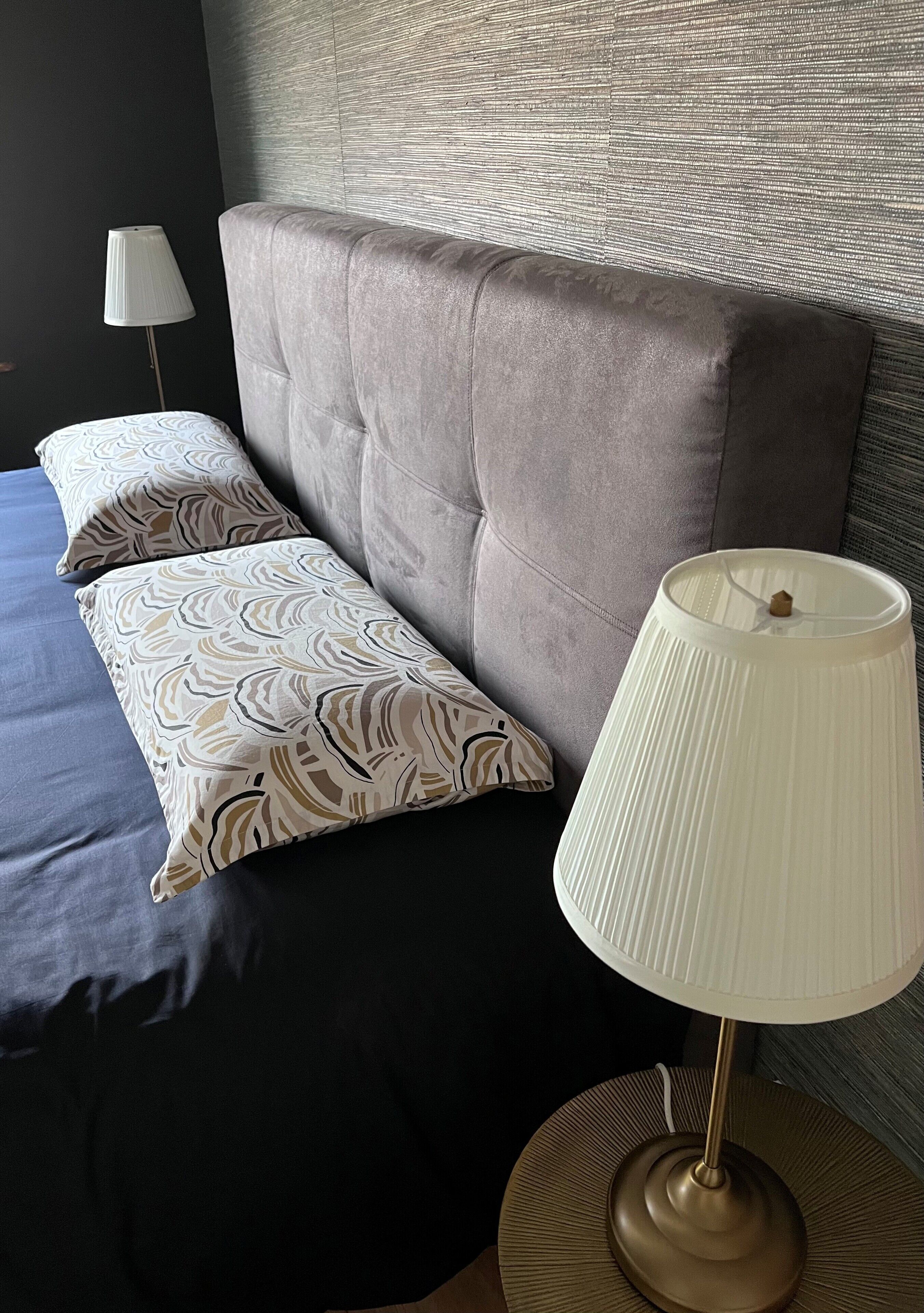 A neatly made bed with patterned pillows, a bedside lamp, and a textured headboard.