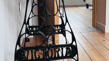 A wrought iron table with a wooden top, placed on a wooden floor in a room with a bed and a window in the background.