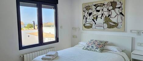 A bedroom with a large bed, a window with a view, and a painting on the wall.