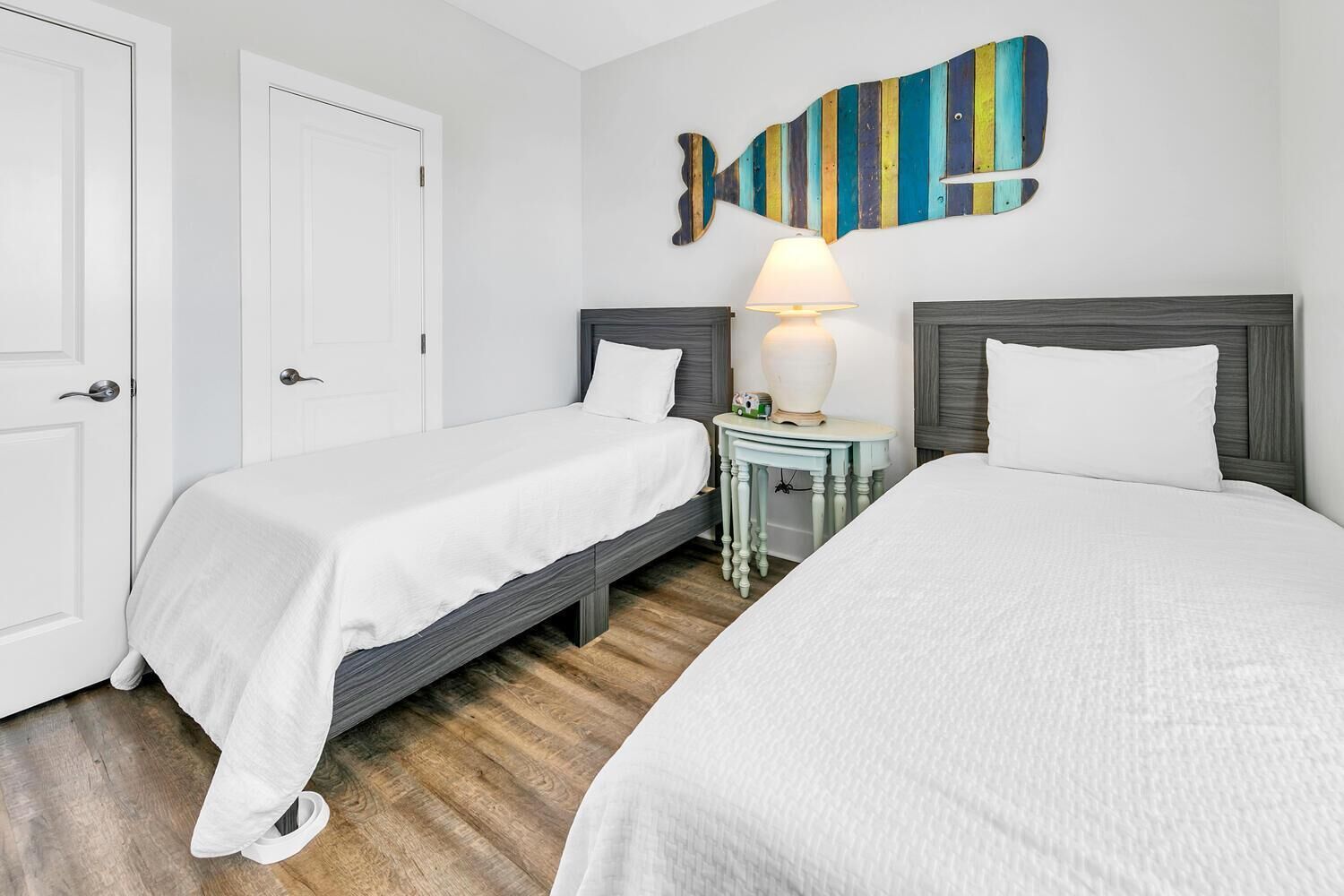 Una habitación de hotel con dos camas individuales, una mesita con una lámpara y un cuadro de peces de colores.